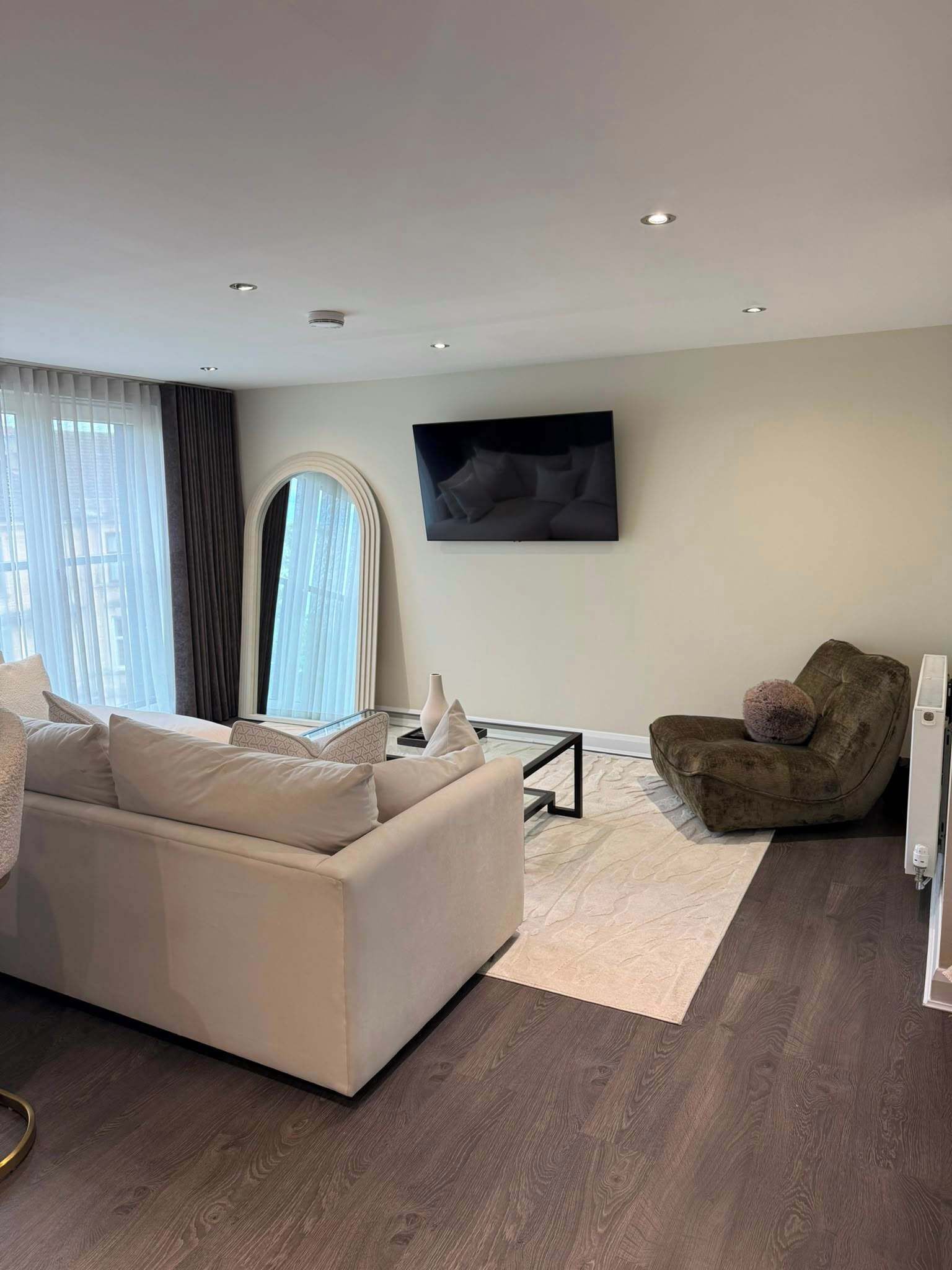 A modern living room with a sofa, armchair, and a flat-screen TV mounted on the wall.