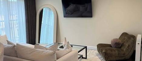 A modern living room with a sofa, armchair, and a flat-screen TV mounted on the wall.