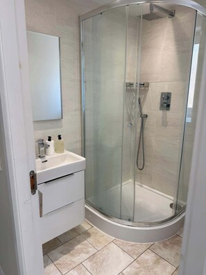A modern bathroom with a glass-enclosed shower, a white sink with a mirror above it, and a door with a handle. - Modern 2 Bed Flat close to Train Station and Hydro (Glasgow City)