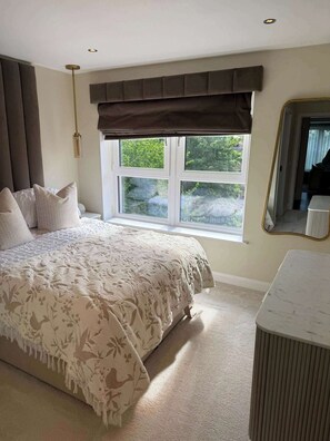 A bedroom with a large bed, a window with a view of greenery, a bedside table, and a mirror. - Modern 2 Bed Flat close to Train Station and Hydro (Glasgow City)