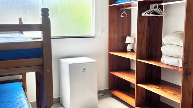 Un dormitori amb una llitera, un aire condicionat blanc, un armari de fusta amb prestatges i un ventilador de sostre.