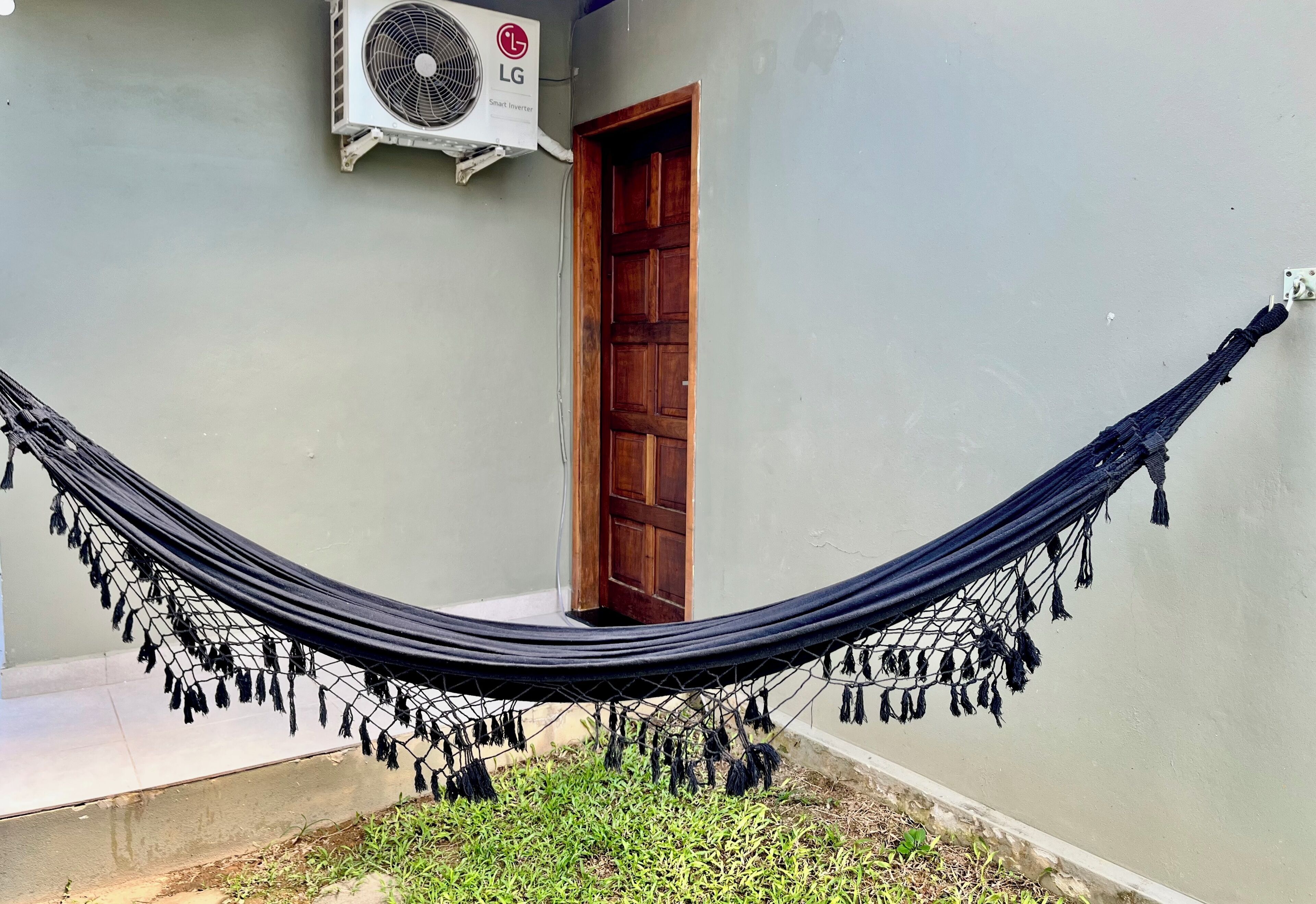 Eine Hängematze, die zwischen zwei Pfosten in einem Innenhof gespannt ist, mit einer Tür und einer an der Wand montierten Klimaanlage.