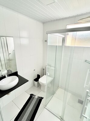 A modern bathroom with a white sink, toilet, and glass-enclosed shower. - Vrbo Property (Ubatuba)