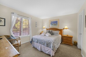 Quarto com cama, luminárias de cabeceira, escrivaninha e janela com persianas.