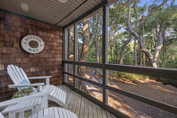 Une terrasse en bois avec des chaises Adirondack et une pancarte indiquant « BIENVENUE À LA PLAGE ».