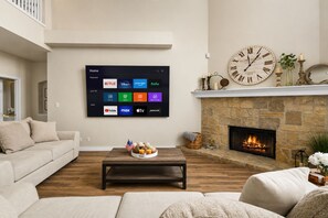 A living room with a large flat-screen TV displaying various streaming services, a stone fireplace with a fire, and a cozy seating arrangement. - SA Family Retreat Near SeaWorld •Six Flags •Lackland w/ EV Charger, BBQ (San Antonio)