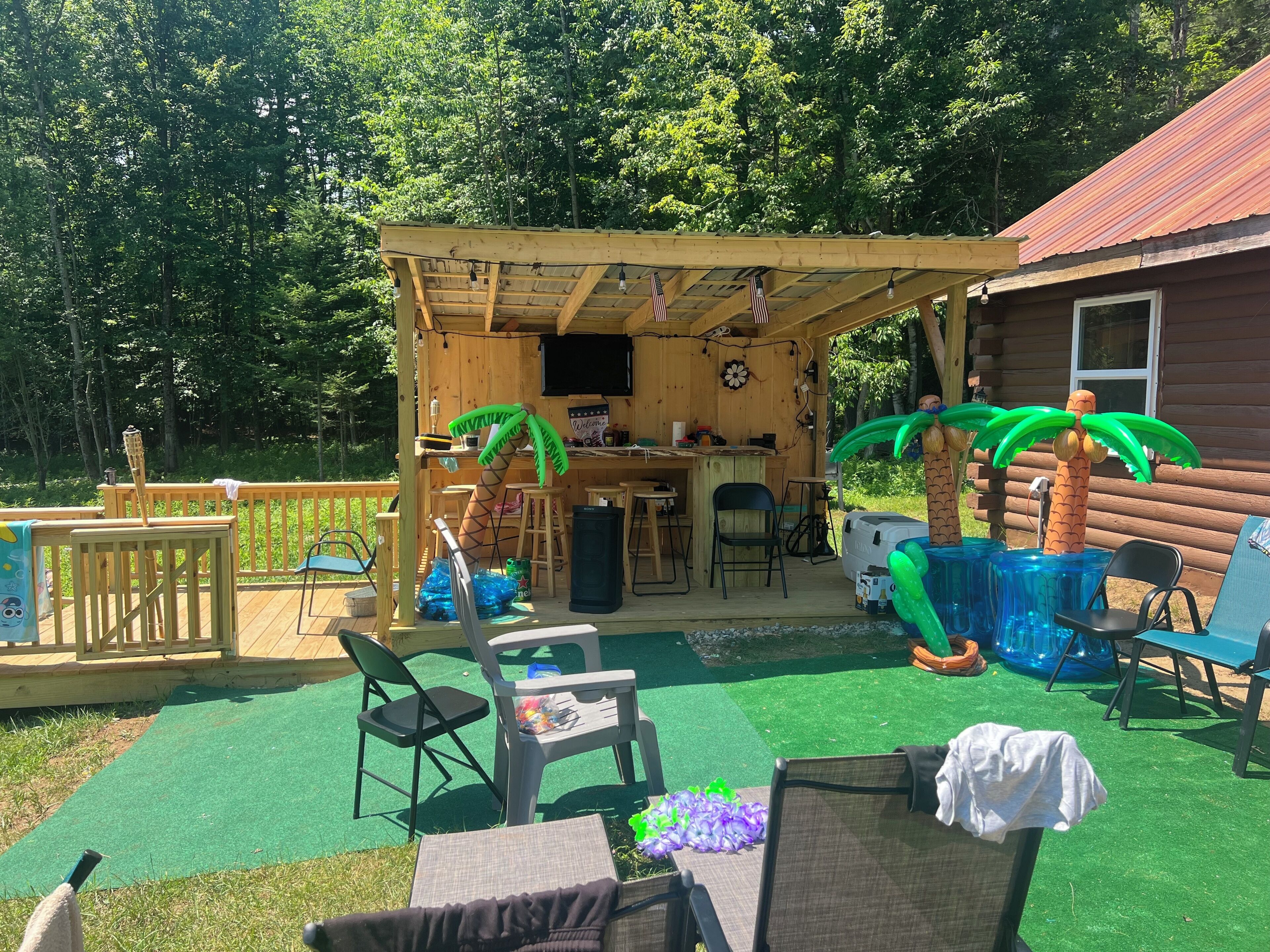 A wooden deck with a covered seating area, outdoor bar, and poolside chairs.