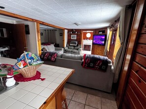 A cozy living room with a fireplace, a television mounted on the wall, and a dining area with a table and chairs. - GORE MT RETREAT. Swimming pool, Hottub, TIKI BAR. FREE SKIPASSES!! (Johnsburg)
