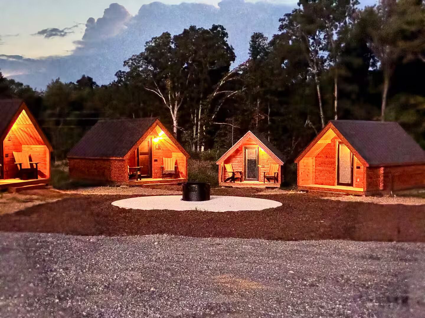 Tres cabañas de madera con chimenea en el centro, rodeadas de árboles.
