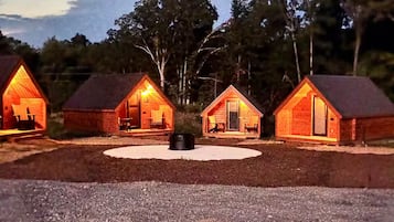Tres cabañas de madera con chimenea en el centro, rodeadas de árboles.