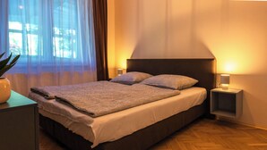 Ein modernes Schlafzimmer mit einem großen Bett, Nachttischlampen und Blick ins Freie durch transparente Vorhänge.
