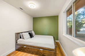 Ein kleines Zimmer mit einem Einzelbett, einem Holzkopfende, einem Fenster und einer Wand in Grüntönen.