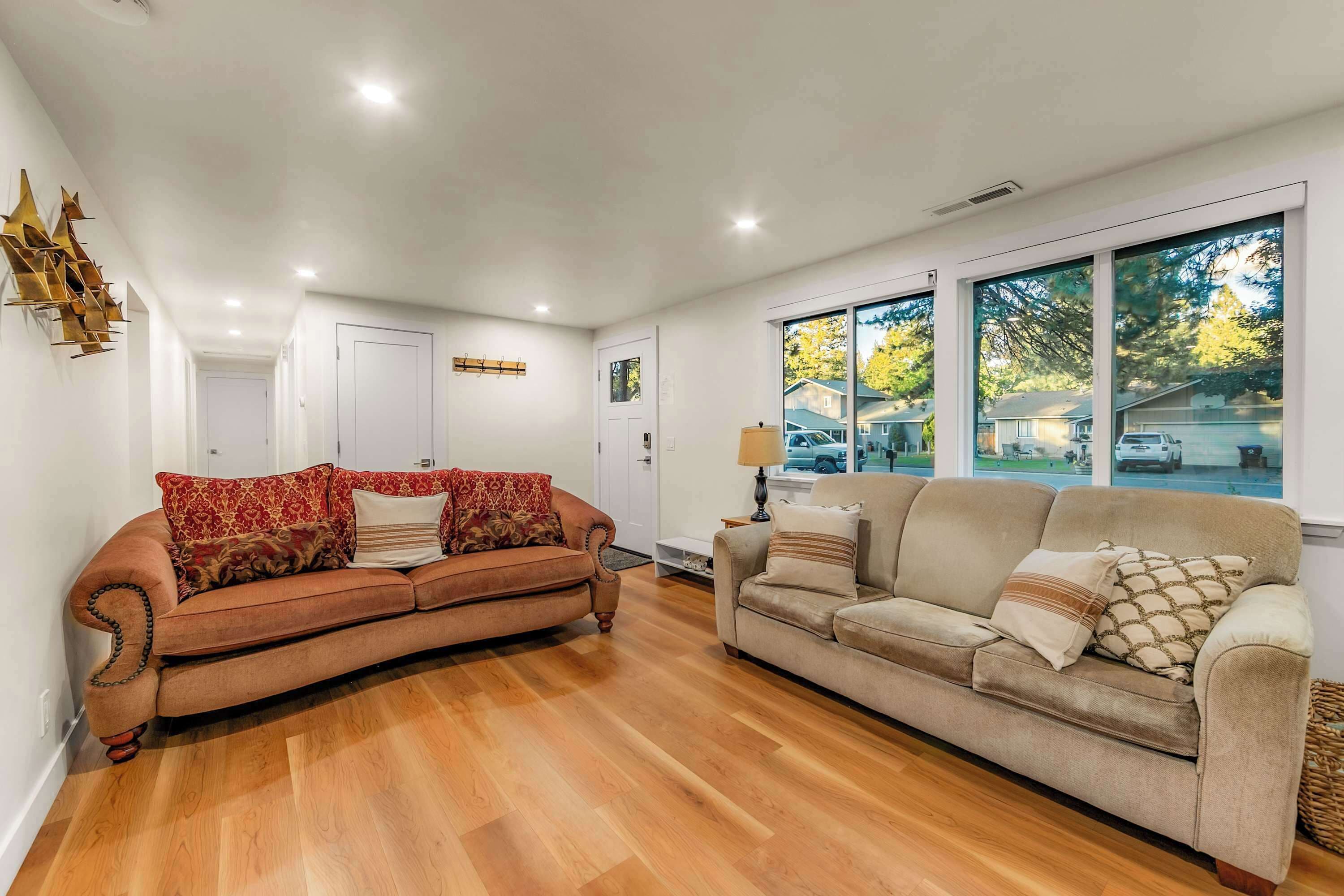 A living room with two sofas, wooden flooring, a white ceiling, and large windows with a view of the outside.