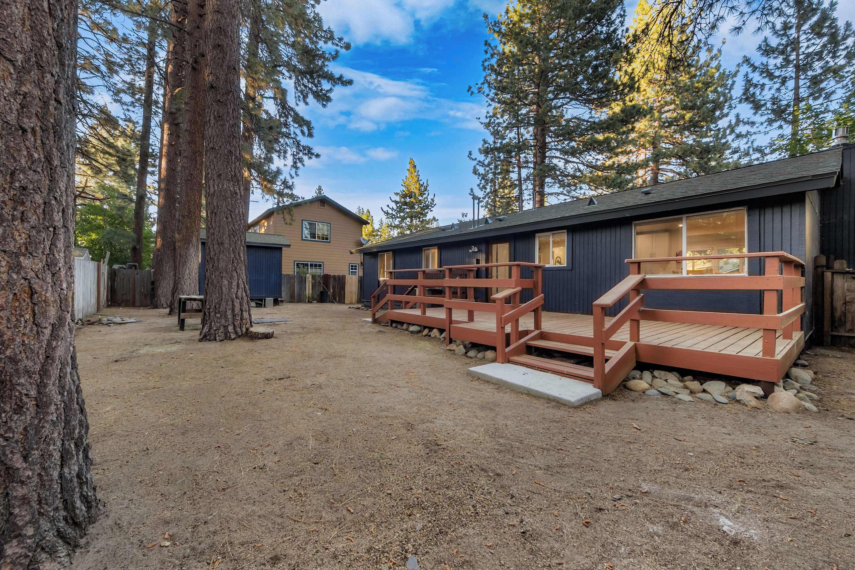 A cabin with a deck and a dirt yard surrounded by trees.