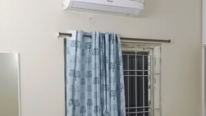 Quarto com cama, mesa de cabeceira, espelho, ar condicionado e janela com cortina.