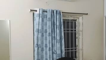 A bedroom with a bed, a nightstand, a mirror, an air conditioning unit, and a window with a curtain.