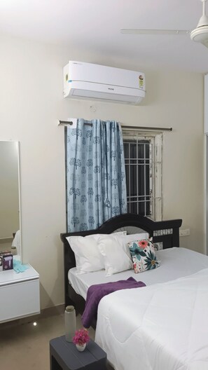 Een slaapkamer met een bed, nachtkastje, spiegel, airconditioning en een raam met gordijn.