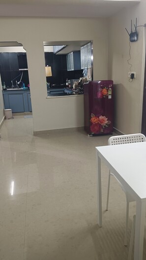 Een keuken met een koelkast, een eettafel en uitzicht op de aangrenzende kamer.