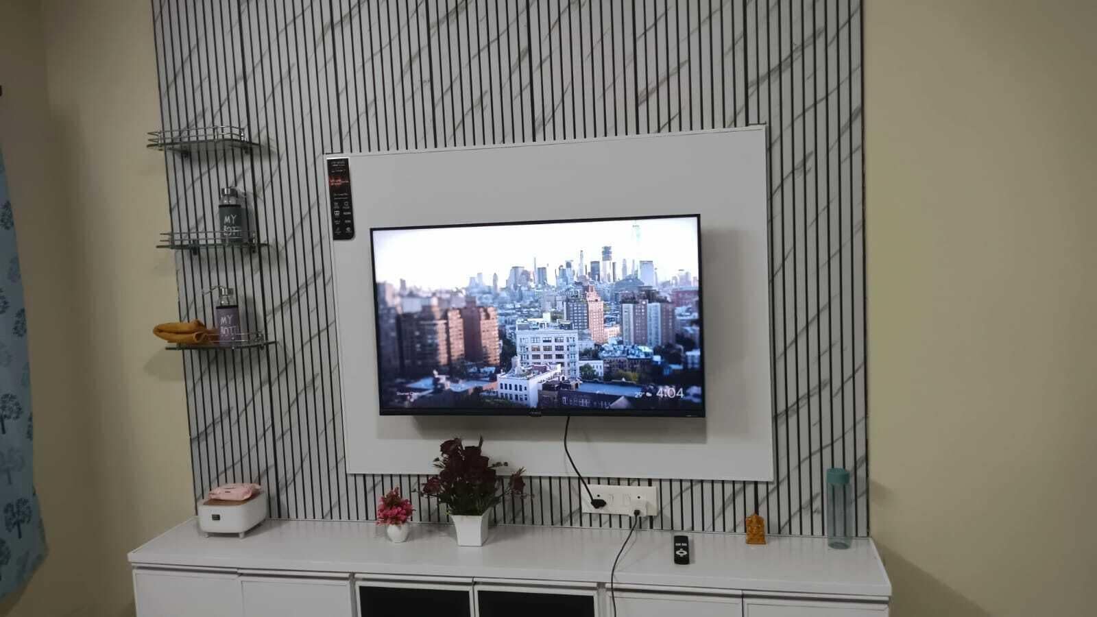A television mounted on a wall with a cityscape on the screen, a white console below, and a plant on the console.