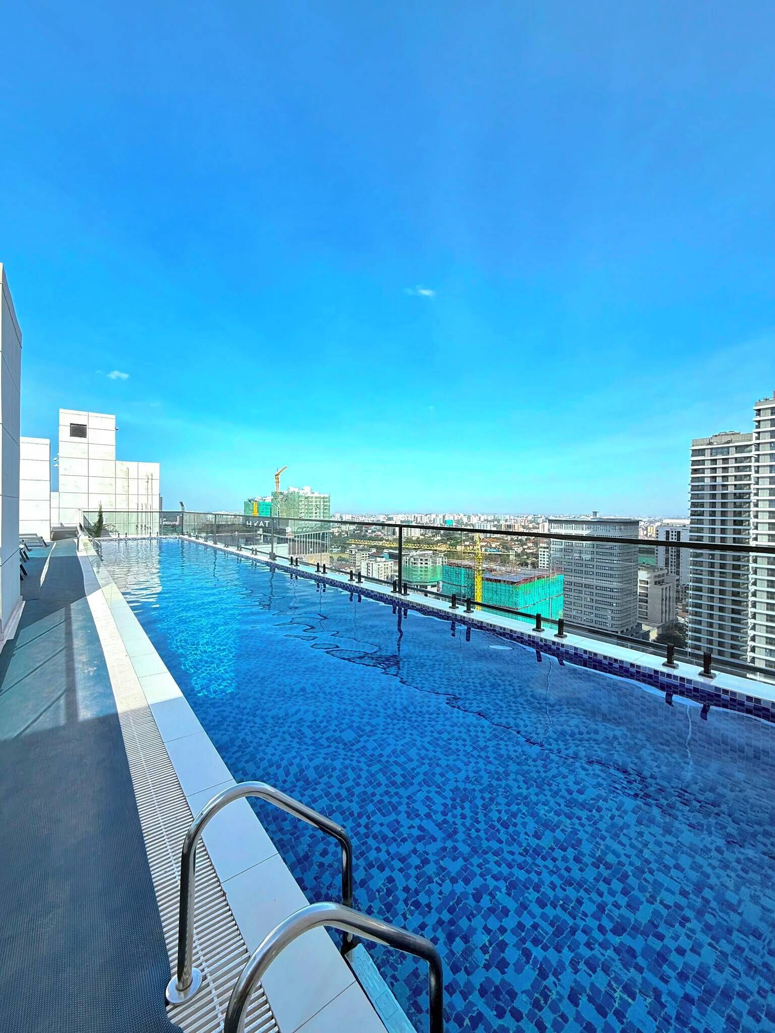 A rooftop swimming pool with a clear view of the cityscape and construction cranes in the background.