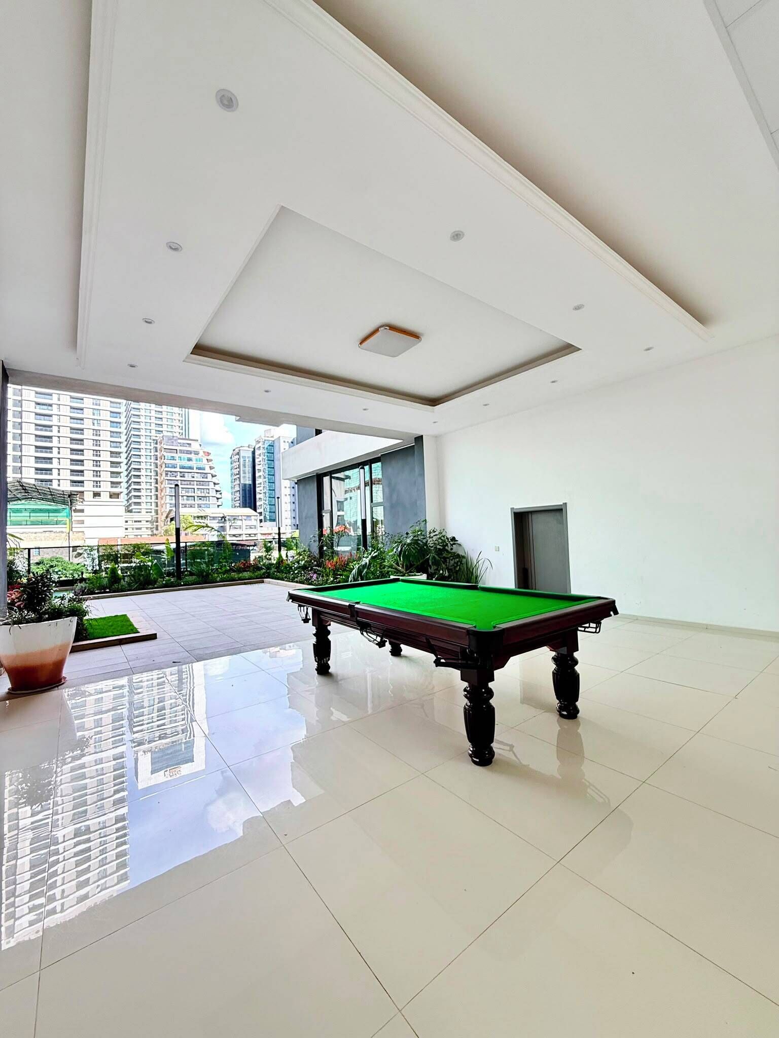 Un espacio interior amplio con mesa de billar, ventanas grandes y vistas a edificios altos.
