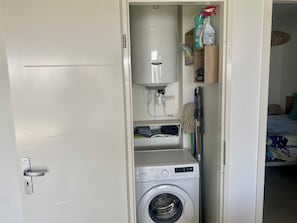 Ein kleiner Waschraum mit Waschmaschine, Warmwasserbereiter und Reinigungsmitteln.