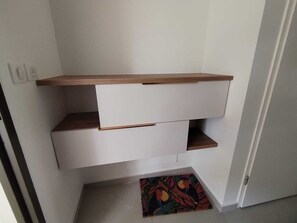 Ein Eckzimmer mit weißer Wand, einem Holzregal und einem weißen Schrank mit Schubladen.