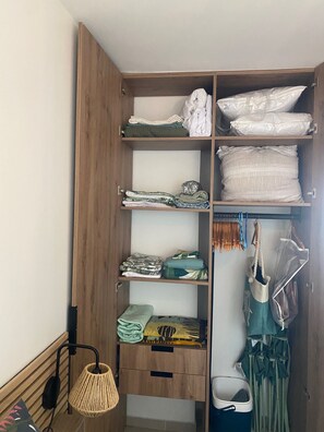 Een houten garderobe met meerdere planken en een kledingroede, gevuld met opgevouwen kleding en tassen.
