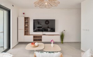 A modern living room with a flat-screen TV mounted on the wall, a wooden cabinet, a round coffee table, and a vase with flowers. - Les Hauts du Green: One-Bedroom Apartment in a Luxury Complex with a Pool Near a Golf Course (Saint-François)