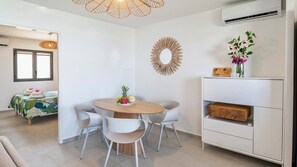 Een moderne kamer met een ronde eettafel, witte stoelen, een witte kast en een bed met een bedspreider met bladprint.