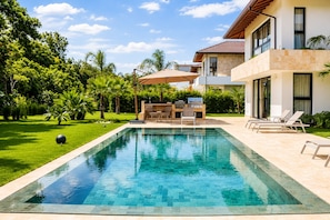 A swimming pool with a barbecue area, surrounded by a well-maintained lawn and tropical plants. - El Bosque II Casa de Campo (La Romana)