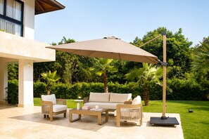 Un patio al aire libre con un sofá color beige, dos sillones, una mesa de centro y un paraguas grande.