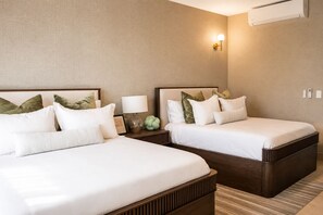 Habitación de hotel con dos camas, una mesita de noche con lámpara y un equipo de aire acondicionado en la pared.
