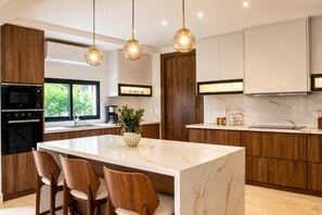 Una cocina moderna con una isla de mármol, armarios de madera e iluminación colgante.