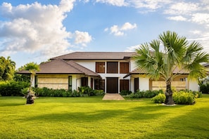 A two-story house with a tiled roof, a front entrance, and a well-maintained lawn with palm trees. - El Bosque II Casa de Campo (La Romana)