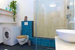 Een badkamer met een wasmachine, toilet en een douchecabine.
