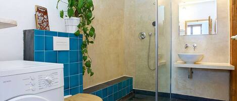 A bathroom with a glass shower enclosure, a white sink, and a washing machine.