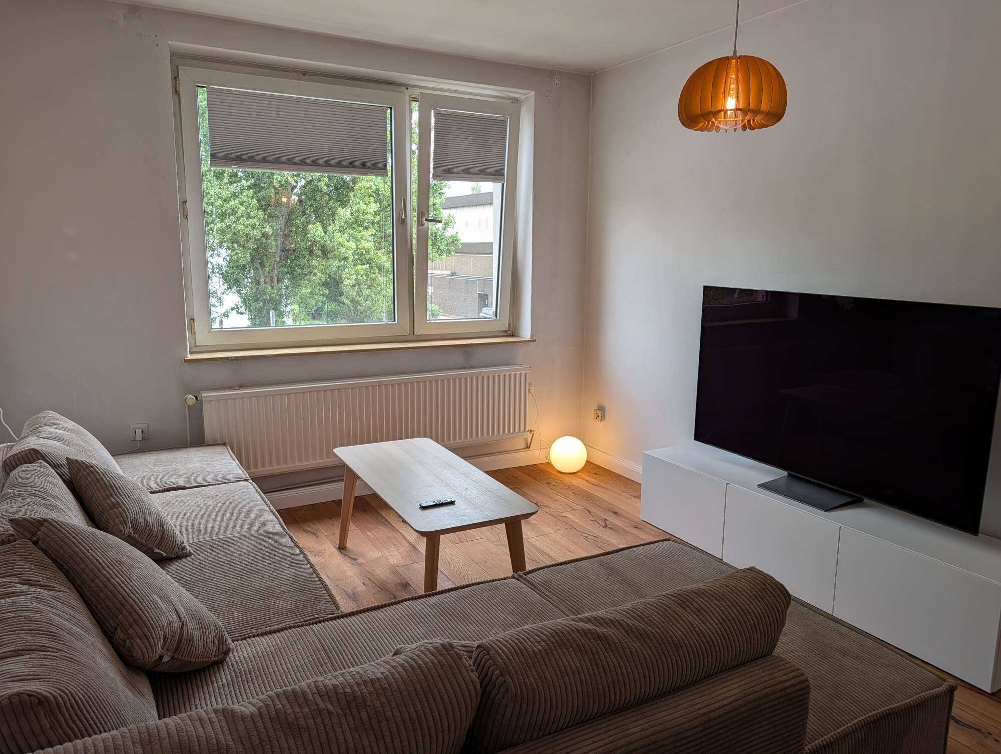 A living room with a sofa set, a coffee table, a TV on a stand, and a window with blinds.