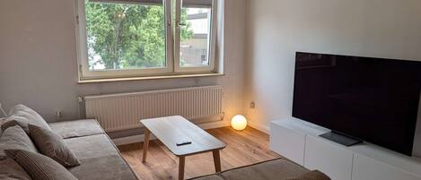 A living room with a sofa set, a coffee table, a TV on a stand, and a window with blinds.