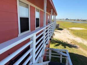 A red building with a white railing and a view of a grassy area and water.