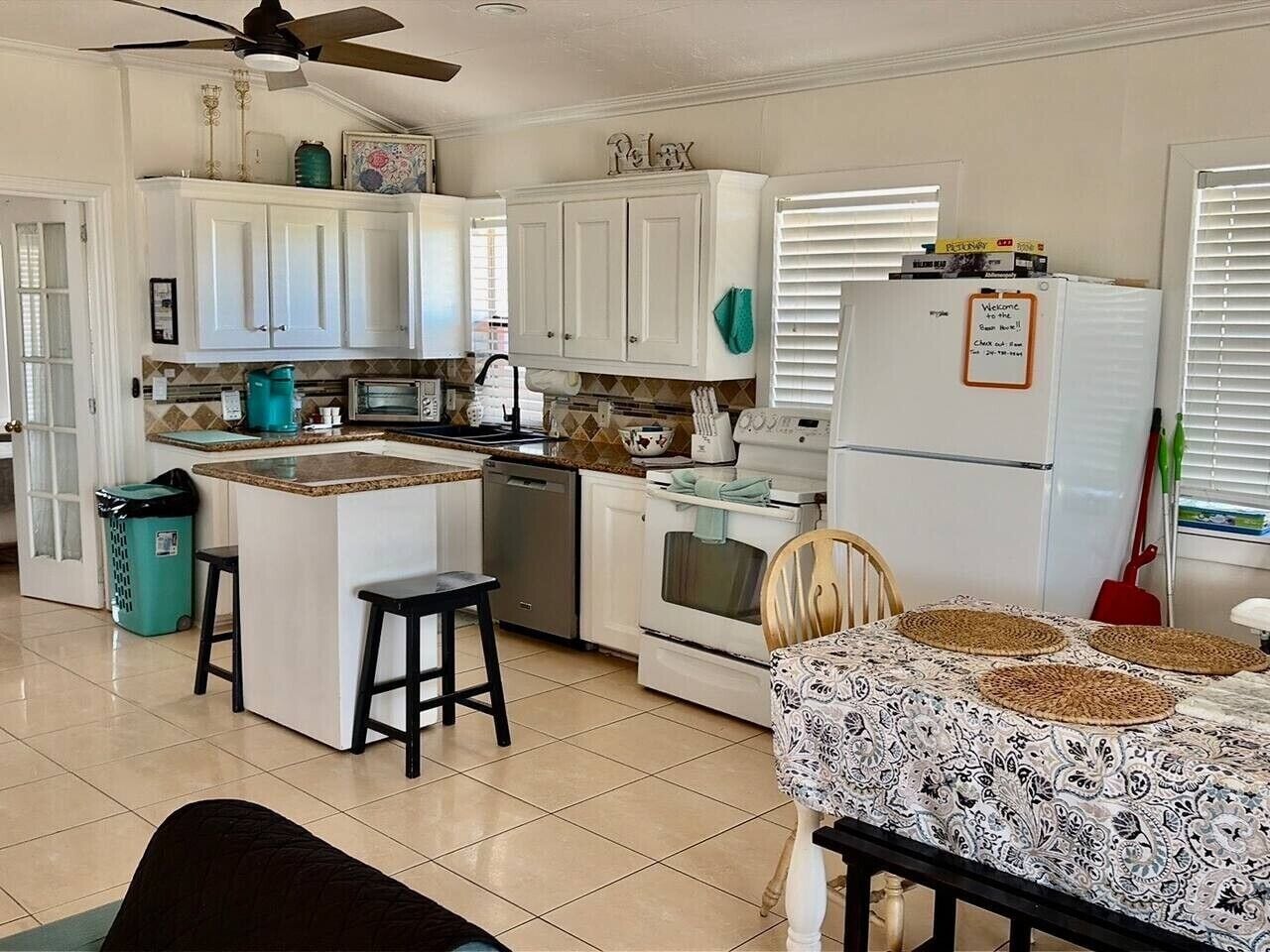 A kitchen with white cabinets, a central island, a refrigerator, and a dining area with a patterned tablecloth.
