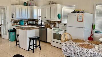 A kitchen with white cabinets, a central island, a refrigerator, and a dining area with a patterned tablecloth.