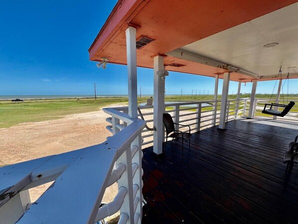 A covered outdoor area with a wooden deck, white railings, and a view of the beach.