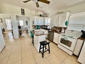 A kitchen with white cabinets, a central island, a stove, and a ceiling fan.