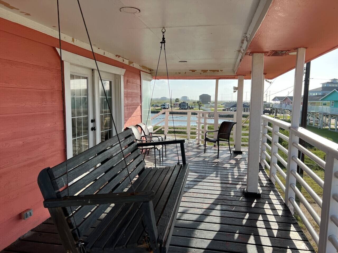 A covered outdoor area with a wooden bench and chairs, a railing, and a view of the surrounding landscape.