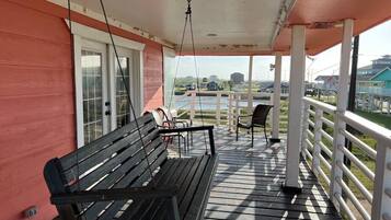 A covered outdoor area with a wooden bench and chairs, a railing, and a view of the surrounding landscape.