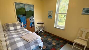 Un dormitorio con cama, una silla, un ventanal y un ventilador de techo.