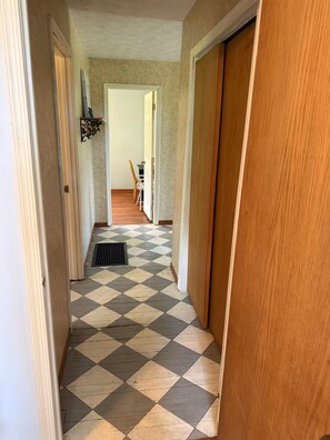 Un pasillo con piso de diseño ajedrezado, puertas de madera y un respiradero en el suelo.
