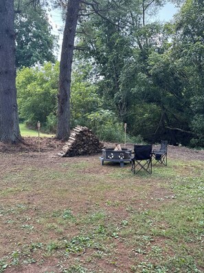Een camping met een vuurkorf, twee stoelen en een stapel hout voor het kampvuur.