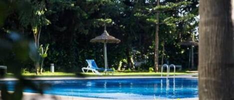Uma piscina com um caminho que a leva, cercada por árvores e um gazebo.